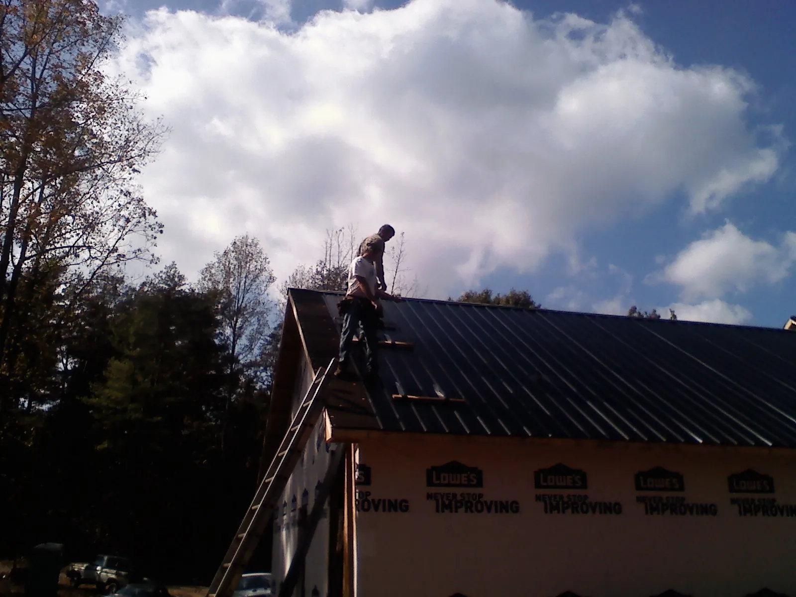 Roofer fastening dark metal panels high against a cloudy sky, from a Roof Inspection job in Coloma
