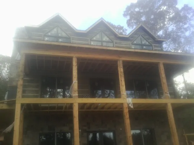Dormers and porch framing on a large log home under construction — Roof Coating work by our crew in Coloma